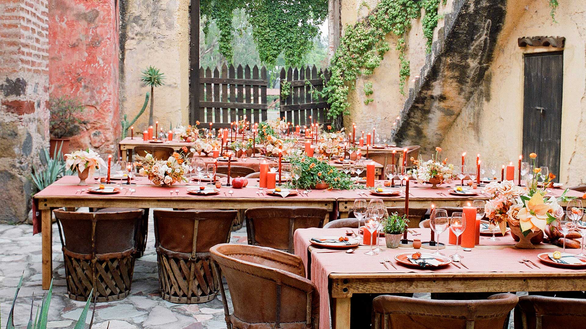 Courtyard event tables set with coral linens, flower arrangements and lit Creative Candles pillar candles
