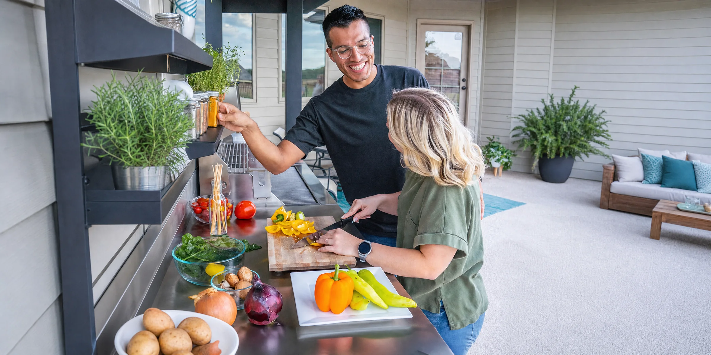 A man and a woman preparing peppers together at an outdoor patio kitchen counter beside their house